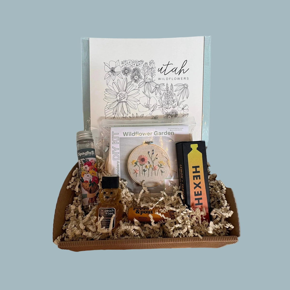 Gift box with stationery items including a card, pen, and cookies on a light blue surface.