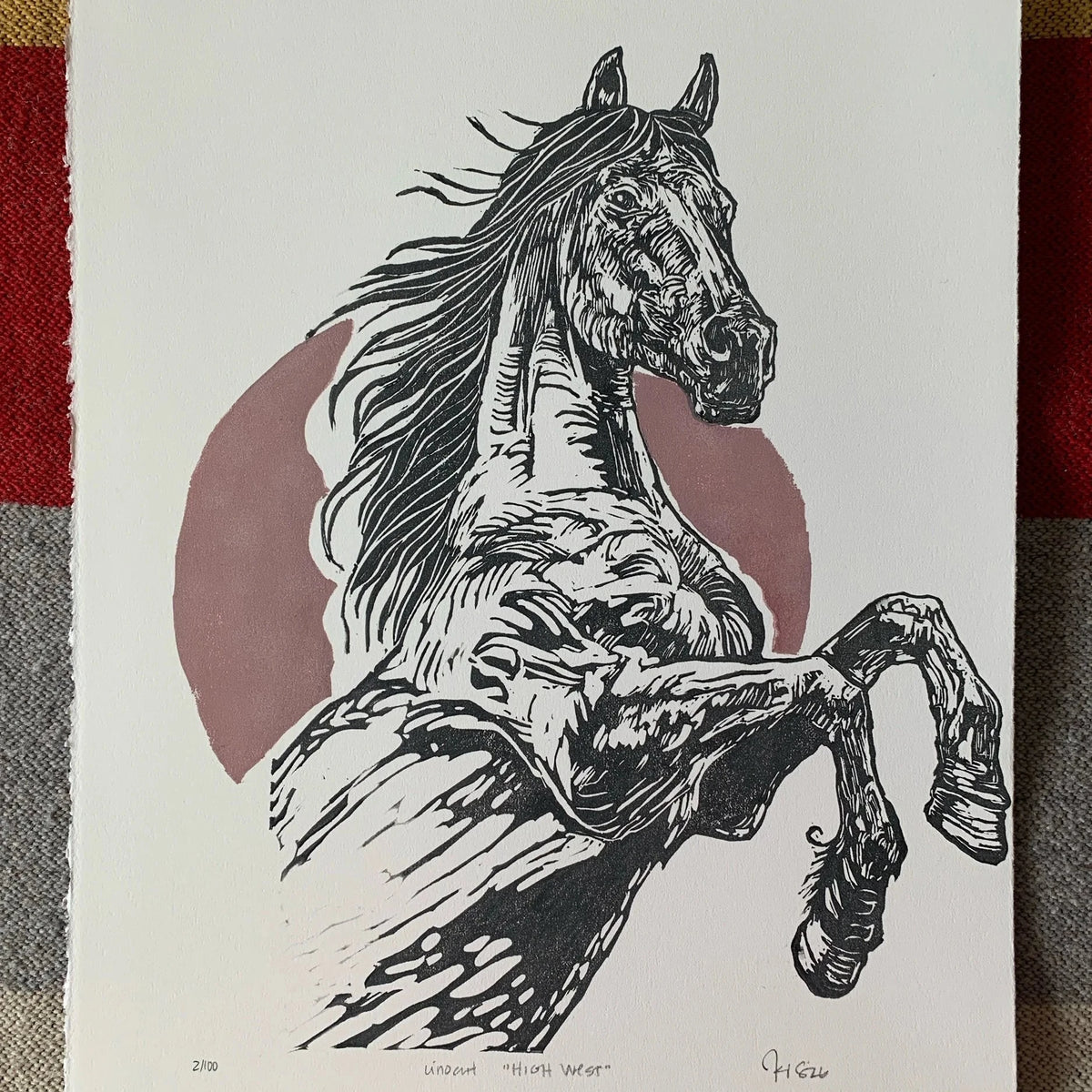 Rearing stallion linocut with red circle in background. Done on rough paper, signed by Kelsi with title and date. Against western rug.