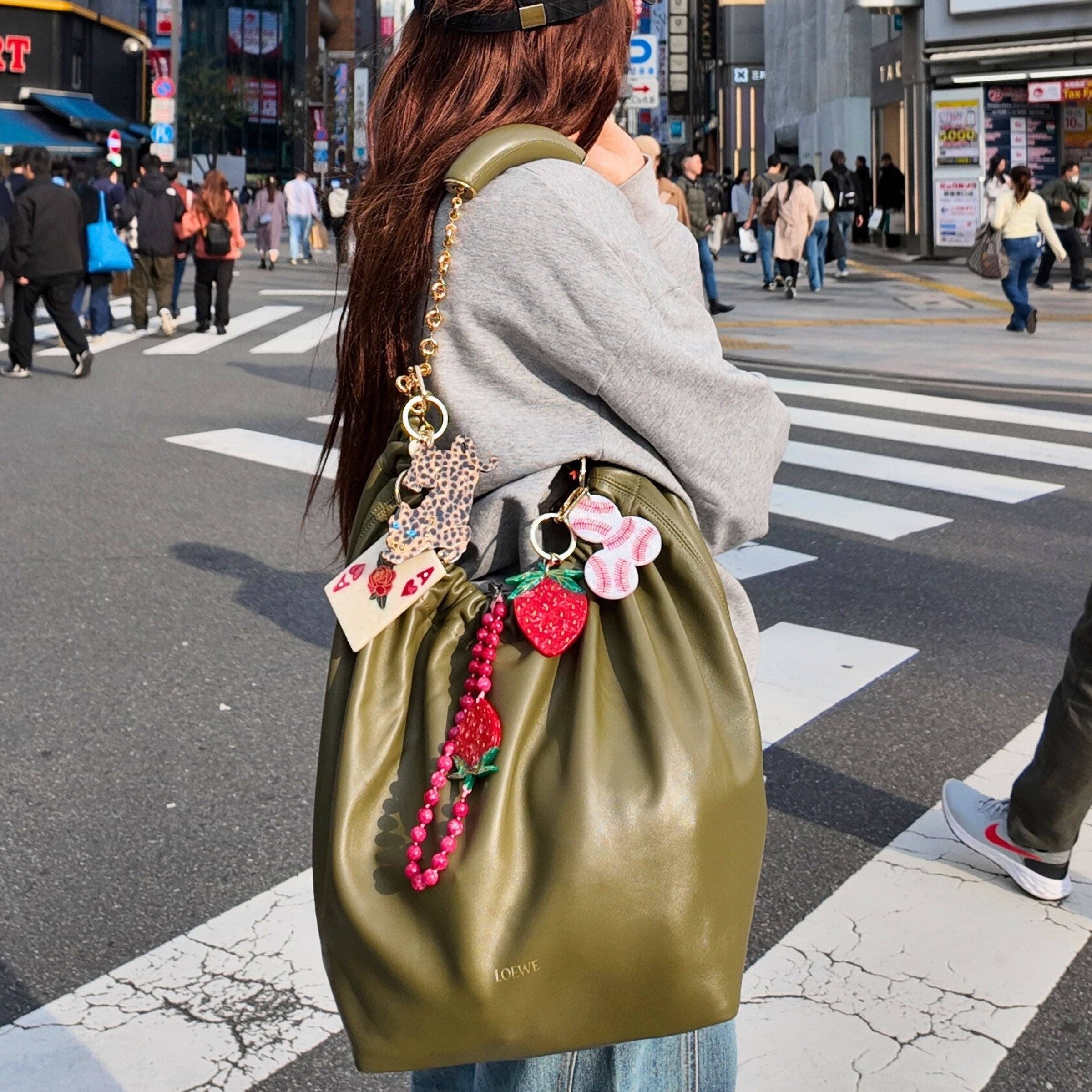 Person with a green bag adorned with colorful charms in a busy urban street.