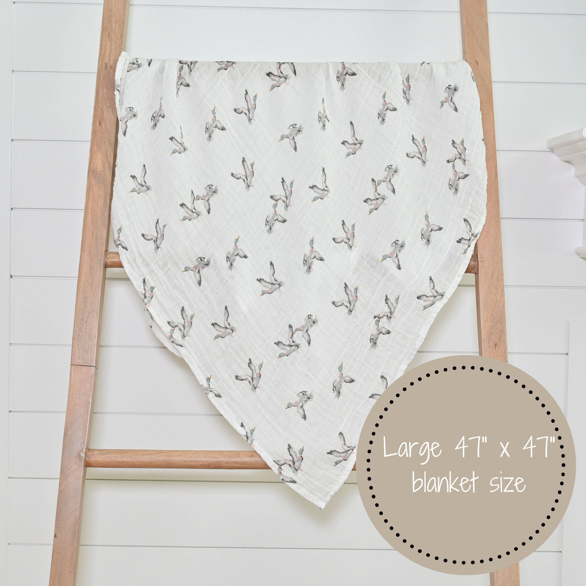 White blanket with black floral pattern draped over a wooden ladder on a white background