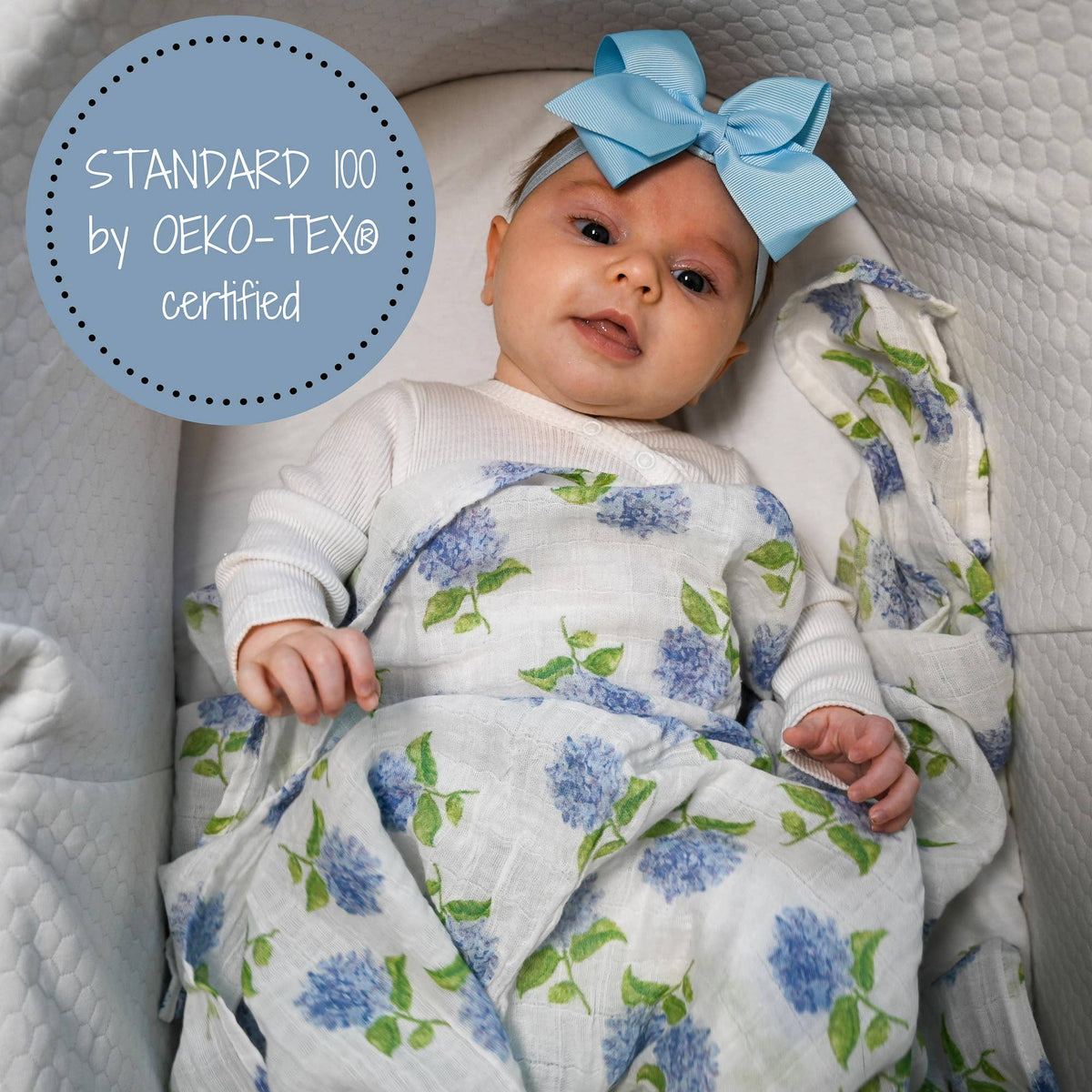 Baby wrapped in a floral blanket with a blue bow, sitting on a textured surface.