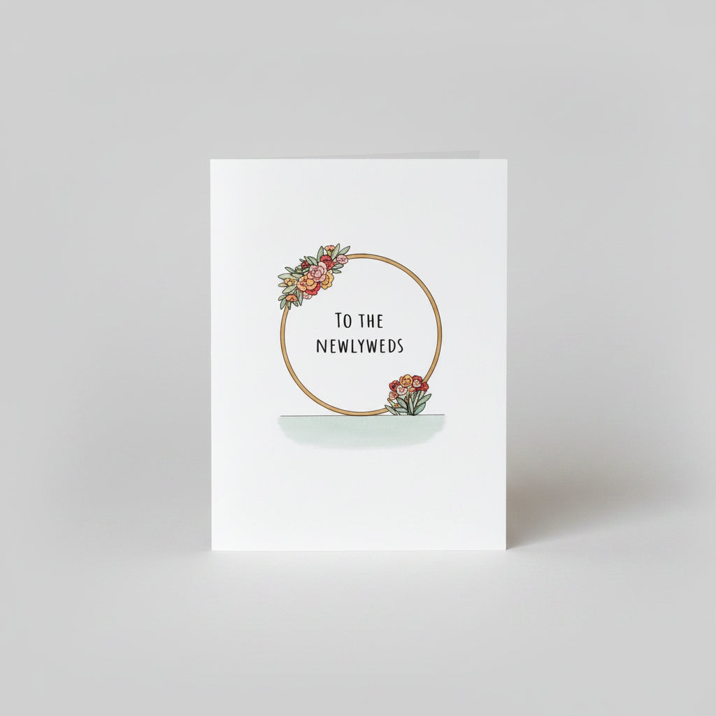 Greeting card with floral design and text 'To the Newlyweds' on a wooden surface