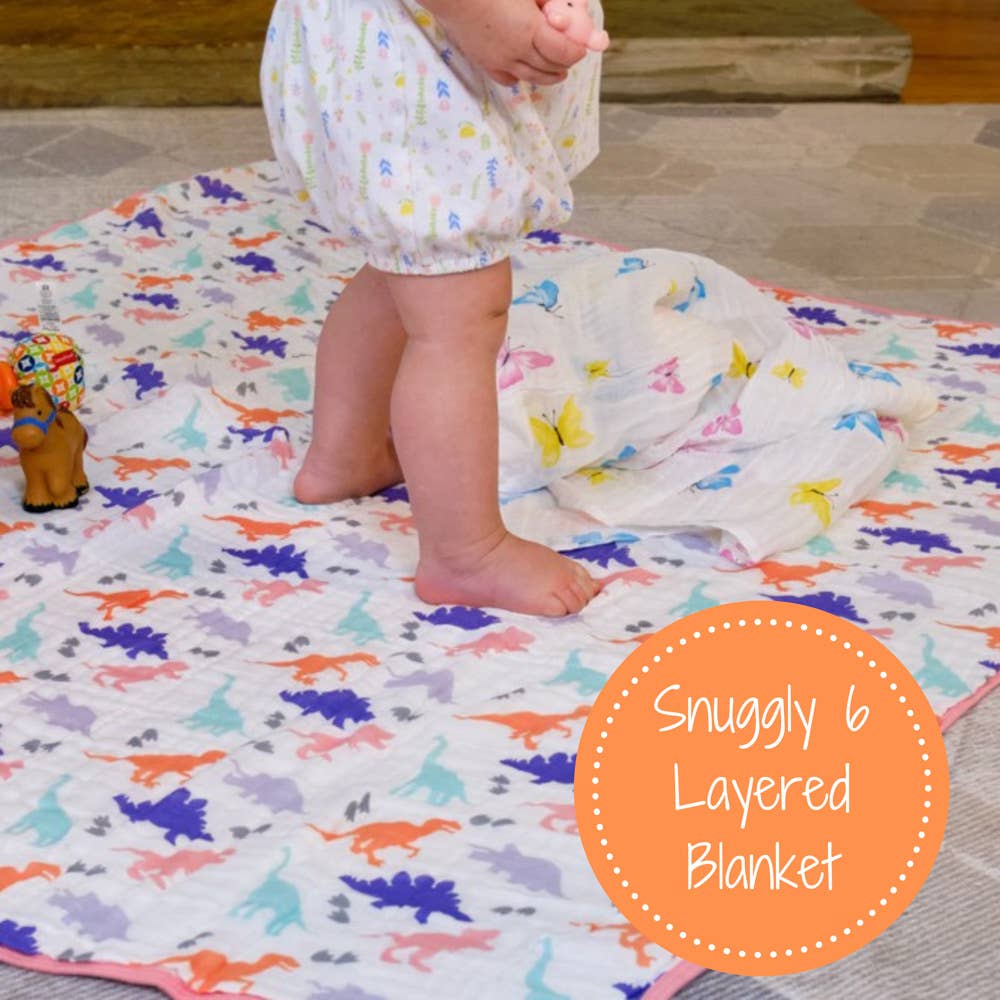 Child playing on a colorful dinosaur-patterned blanket with 'Snuggly 6 Layered Blanket' text overlay.