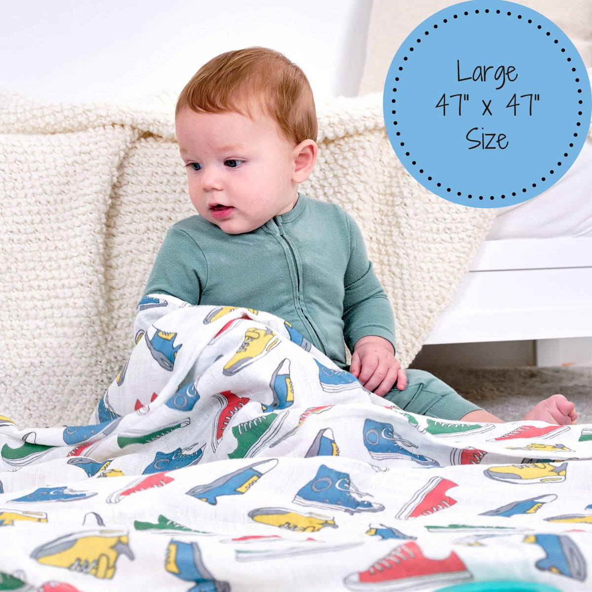 Baby sitting on a couch with a large blanket featuring colorful shoe patterns, with text indicating size.