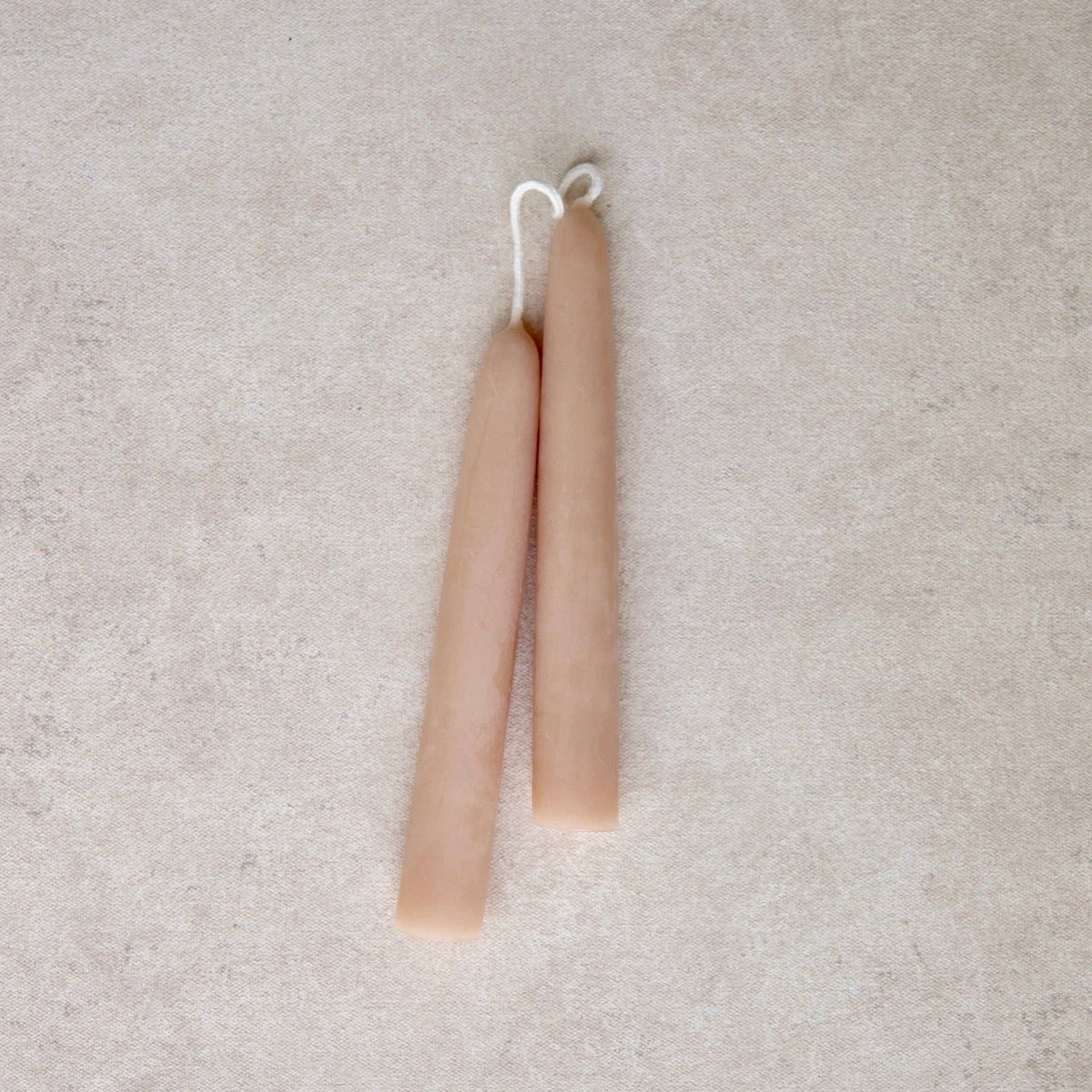 Two slim, tapered candles in a light rose color, arranged vertically side-by-side on a textured light gray surface.