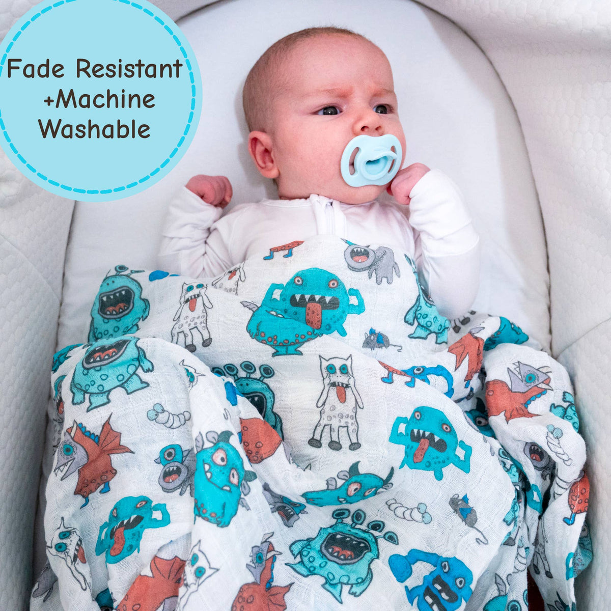 Baby wrapped in a blanket with monster pattern, wearing a blue pacifier, on a white background.