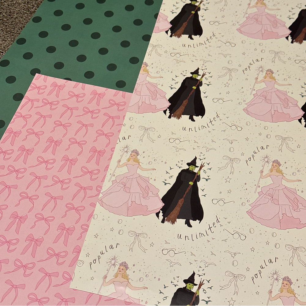 Example swatch of Wicked wrapping paper, showing full design. Glinda and Elphaba in their iconic outfits, surrounded by bubbles, sparkles, bows, and Oz spectacles.