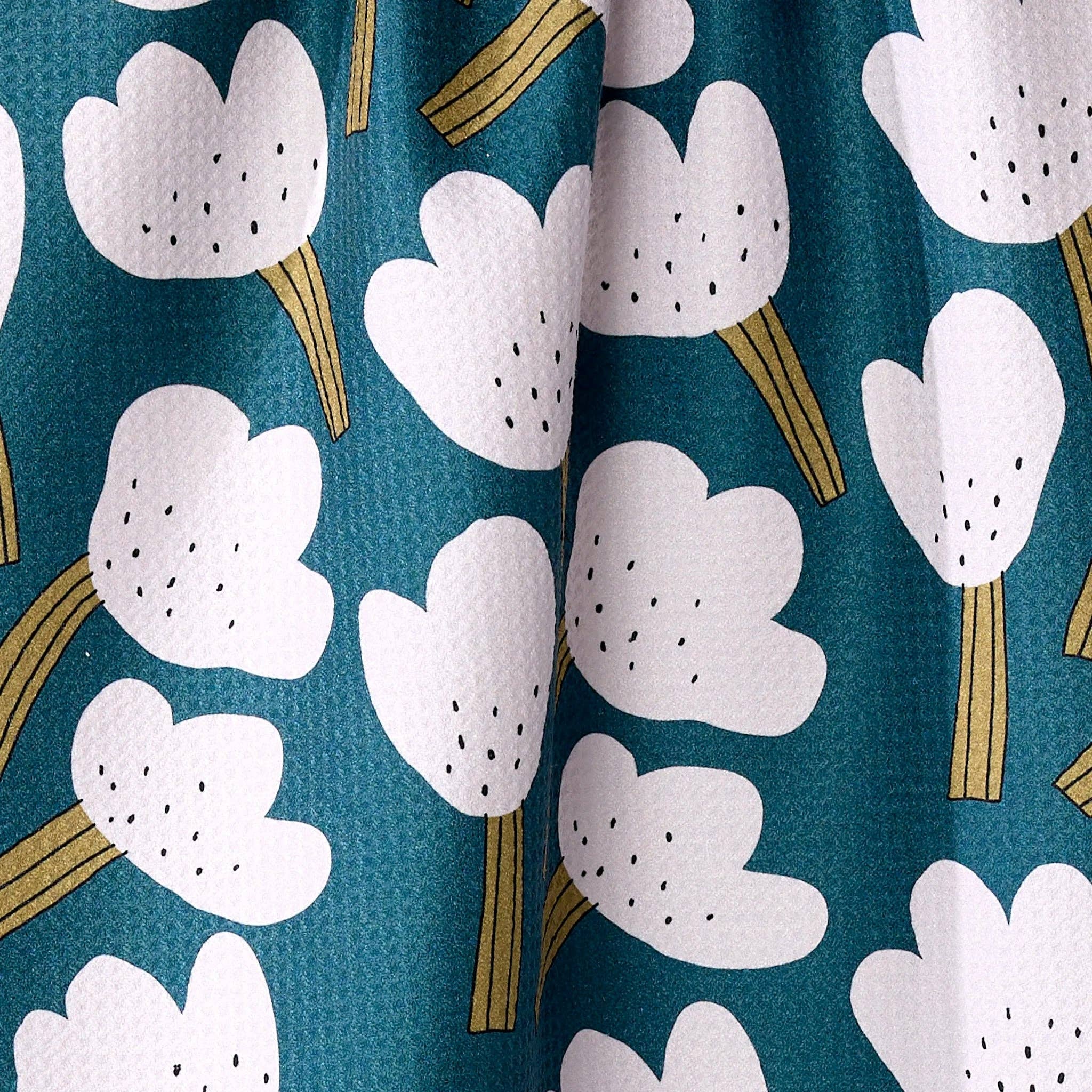 white tea towel floral pattern on a teal background hanging against a plain wall.