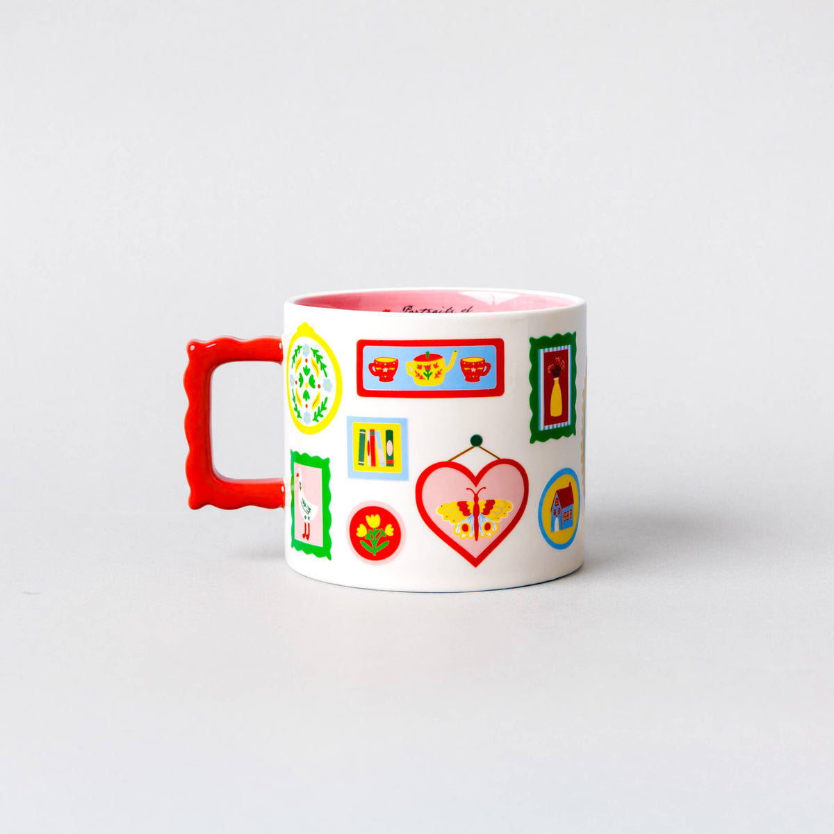 A white ceramic mug with a bright red handle and a pink interior, decorated with colorful cartoon-style icons and frames on the side, set against a plain light gray background.