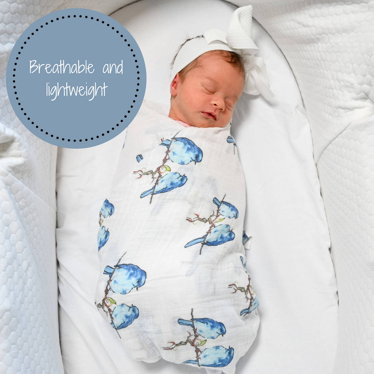 A sleeping newborn baby swaddled in a white muslin blanket with a blue bird print, resting on a white bassinet. A blue circular graphic overlay in the top left reads 'Breathable, and lightweight'.