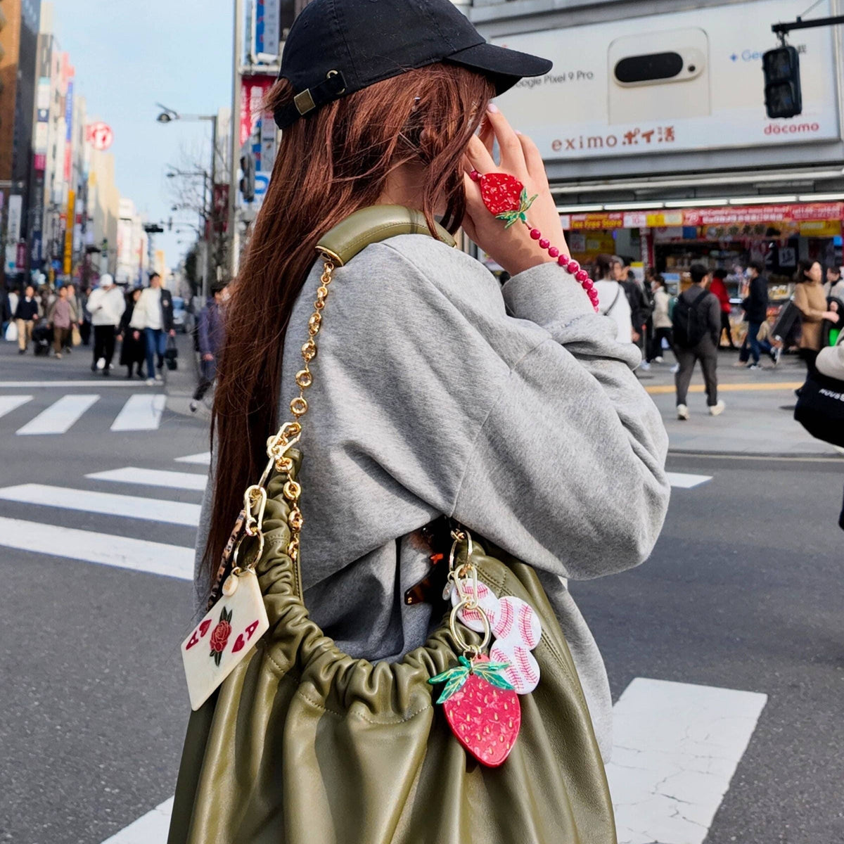 Person with a green bag featuring strawberry charms in an urban setting