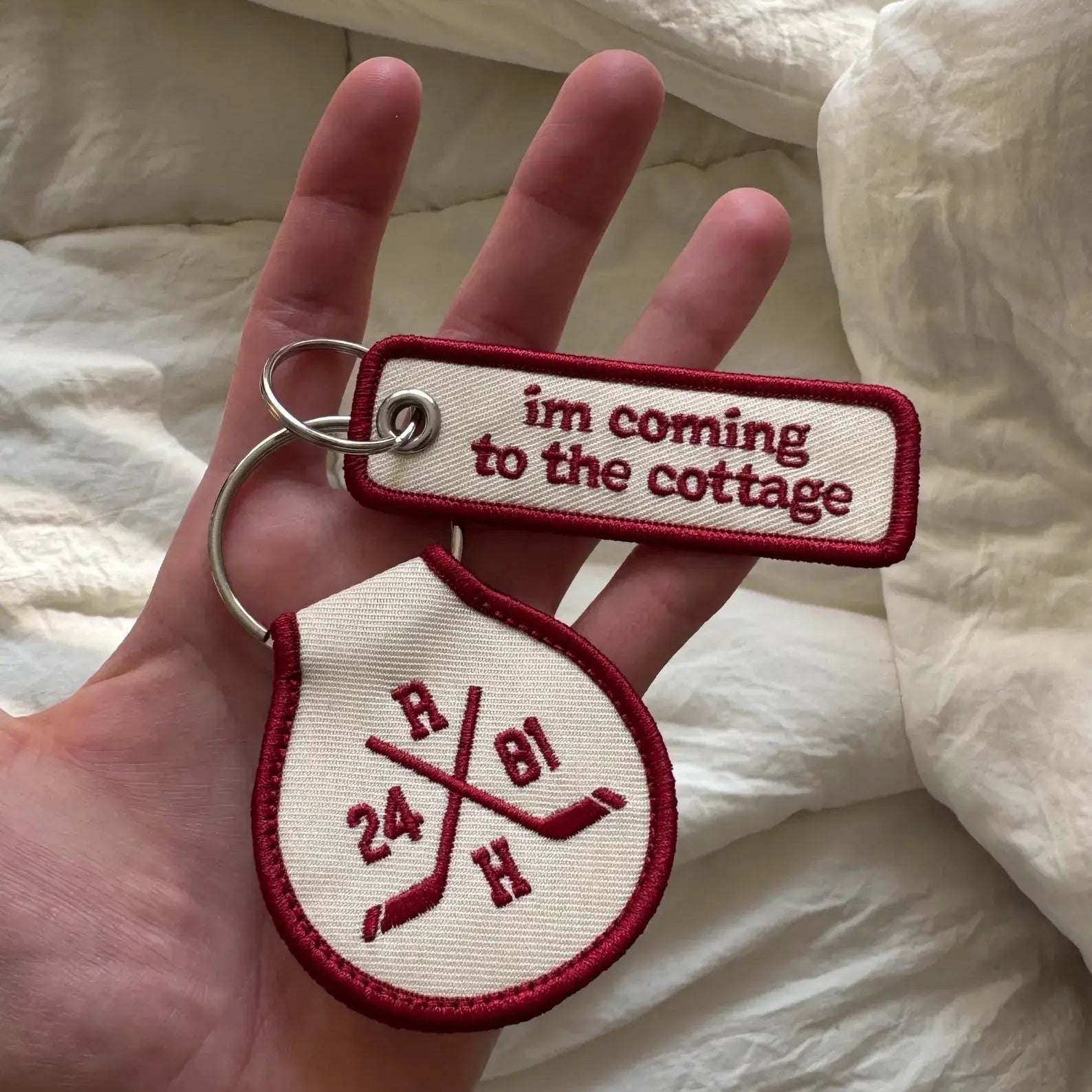 Two keychains held in a hand with text and symbols on a white fabric background