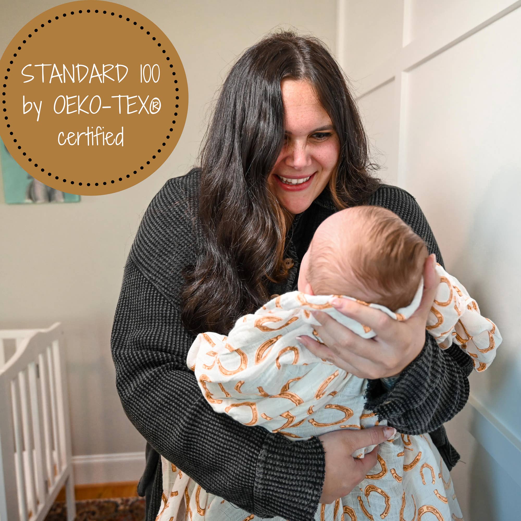 Woman holding a baby wrapped in a patterned blanket with 'Standard 100 by OEKO-TEX® certified' label.