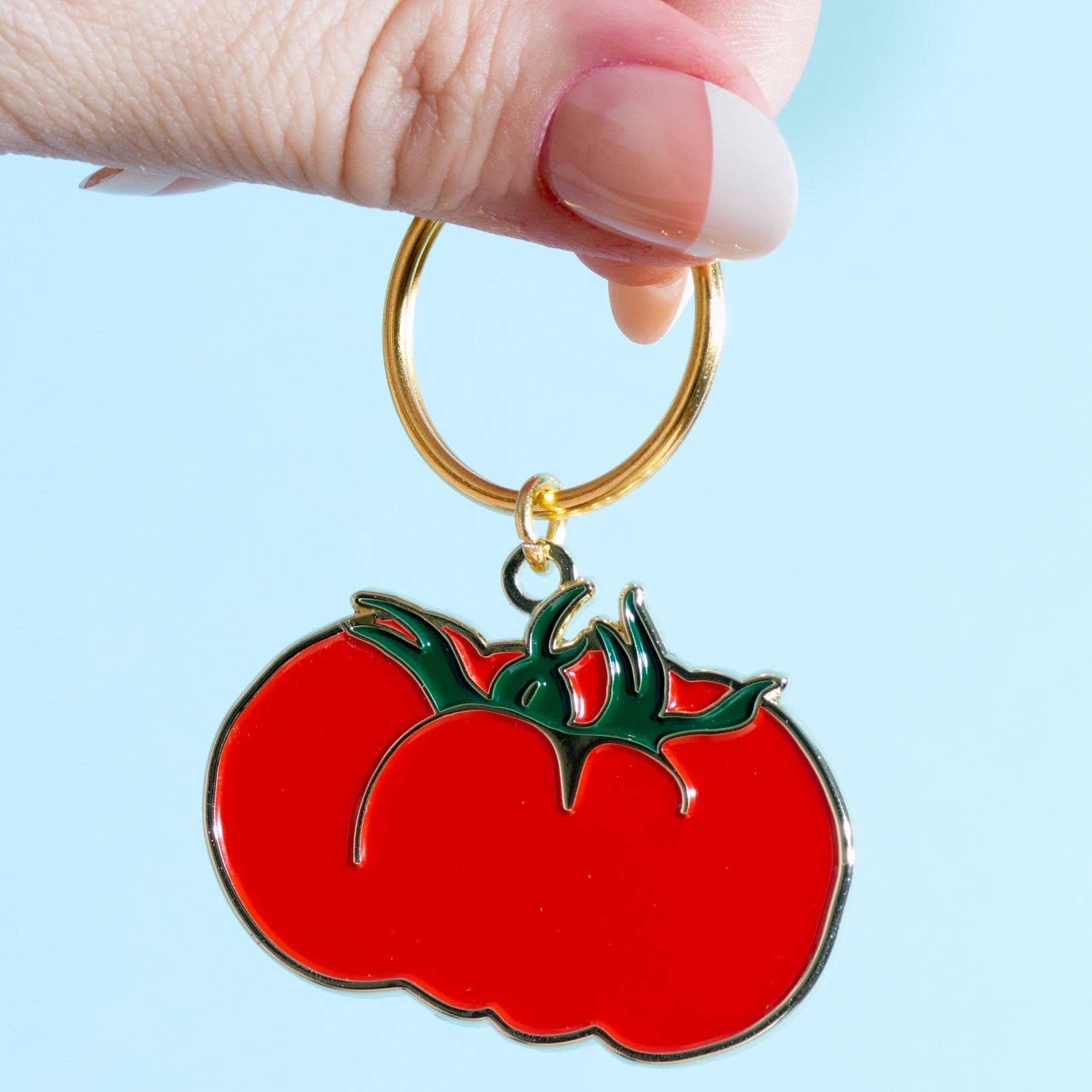 Keychain shaped like a tomato held by a hand against a light blue background