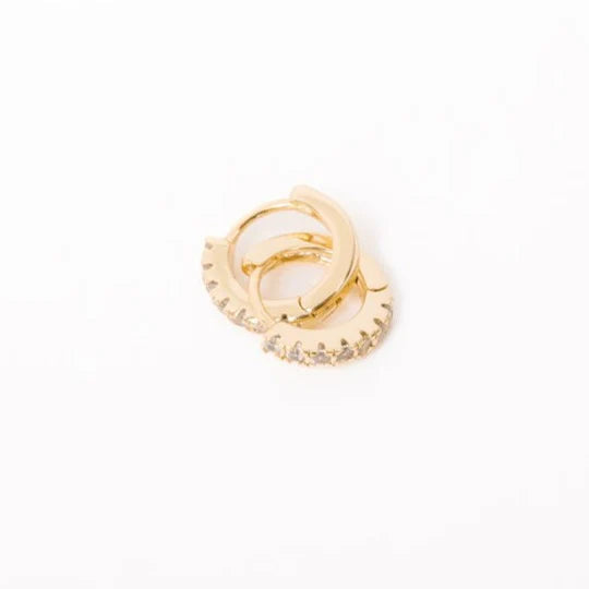 A pair of gold huggie hoop earrings with cubic zirconia stones, displayed against a white background.