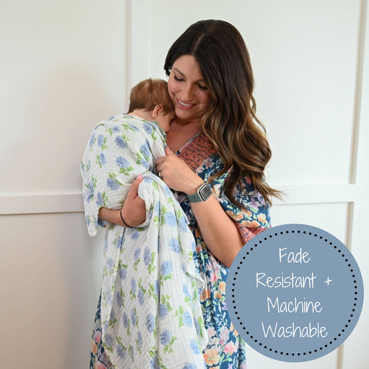 Woman holding a baby wrapped in a floral blanket with text 'Fade Resistant + Machine Washable' on a white background.