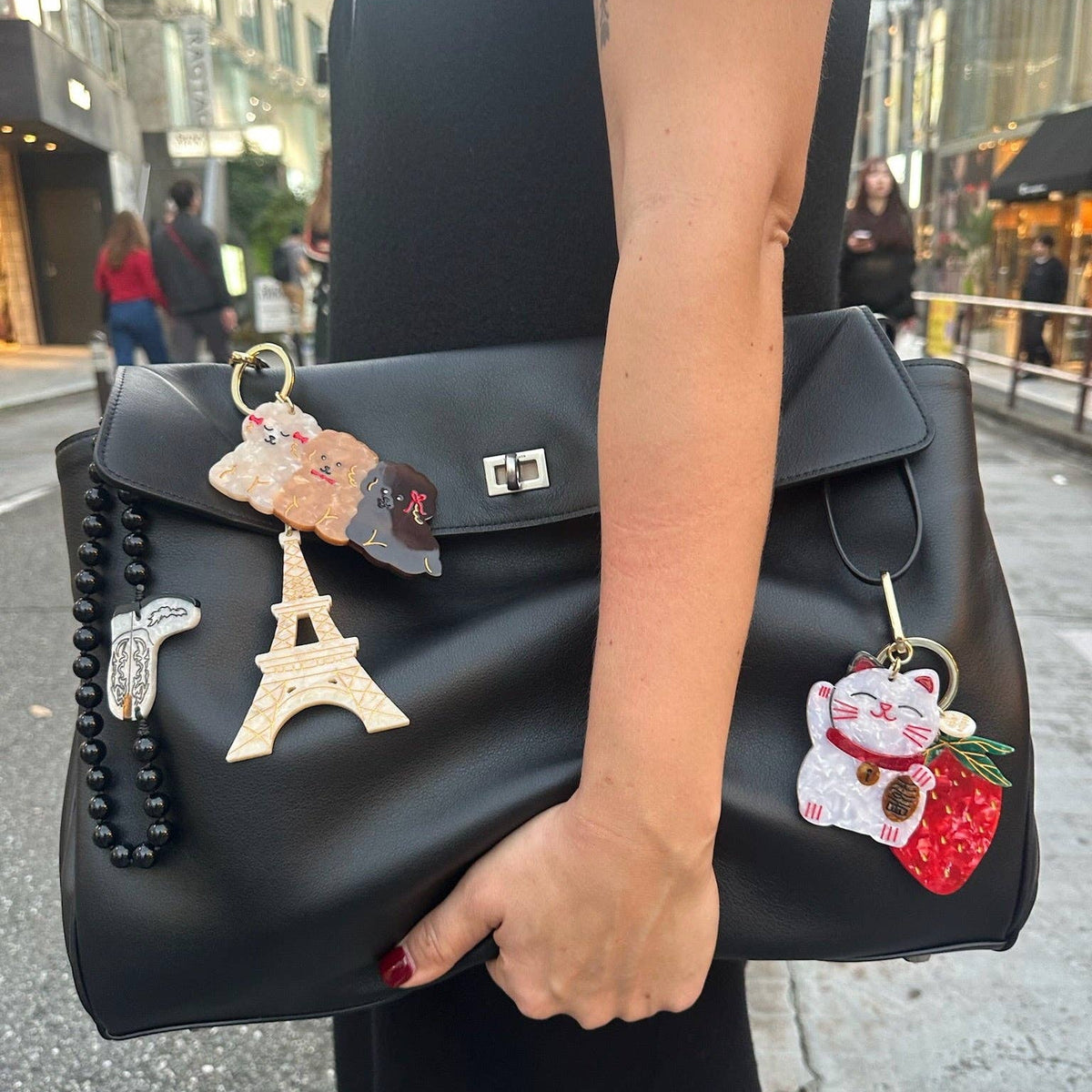 Person holding a black handbag with decorative charms in an urban setting