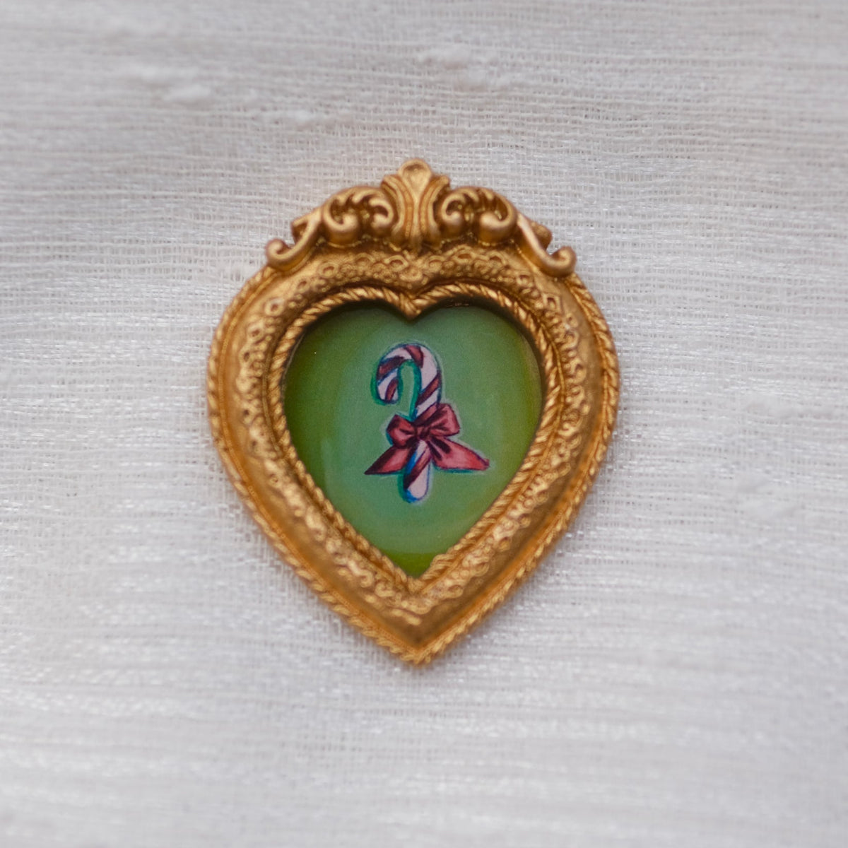 A painting of a candy cane with bow tied around it in a framed magnet.