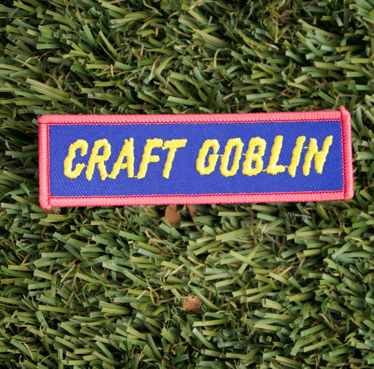 Iron-on rectangular shaped patch with a red border, blue background and yellow words that say "Craft Goblin".