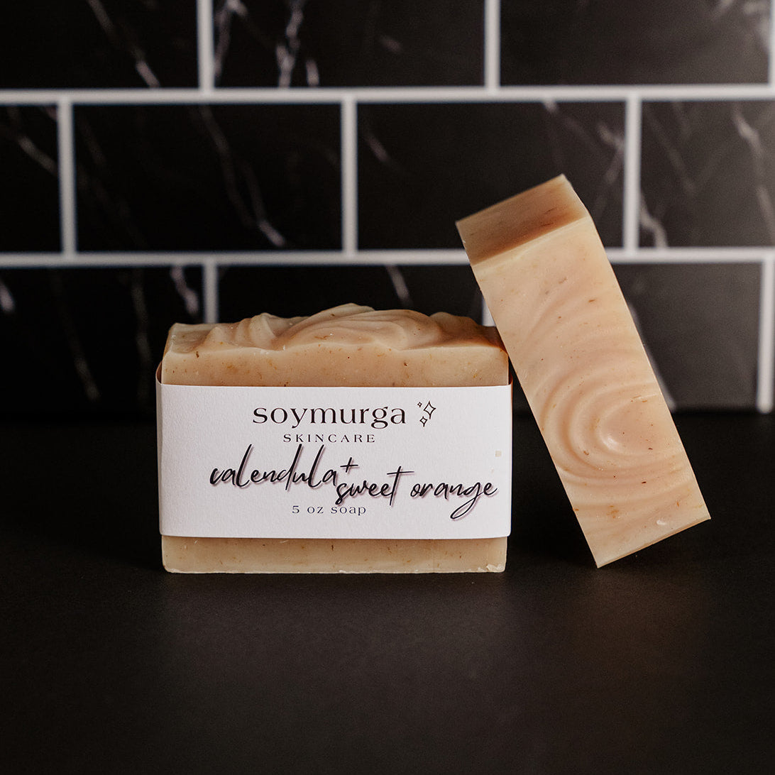 Calendula + Sweet Orange soap bar on a black countertop with black marble subway tile in the background.