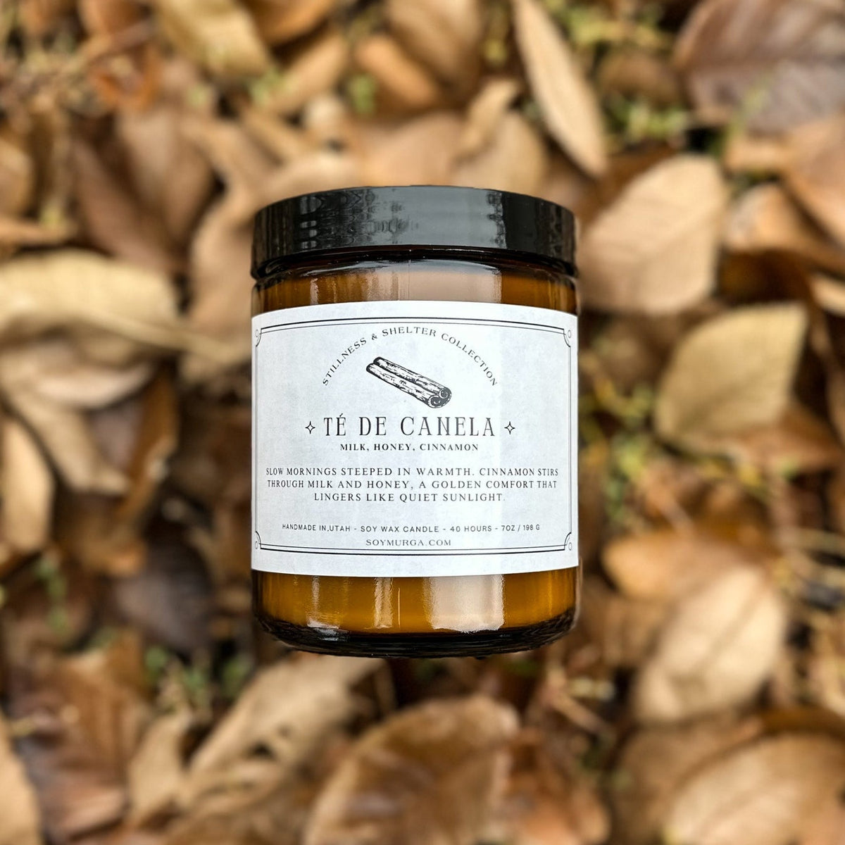 Te De Canela candle in an amber glass laying atop a pile of fall leaves.