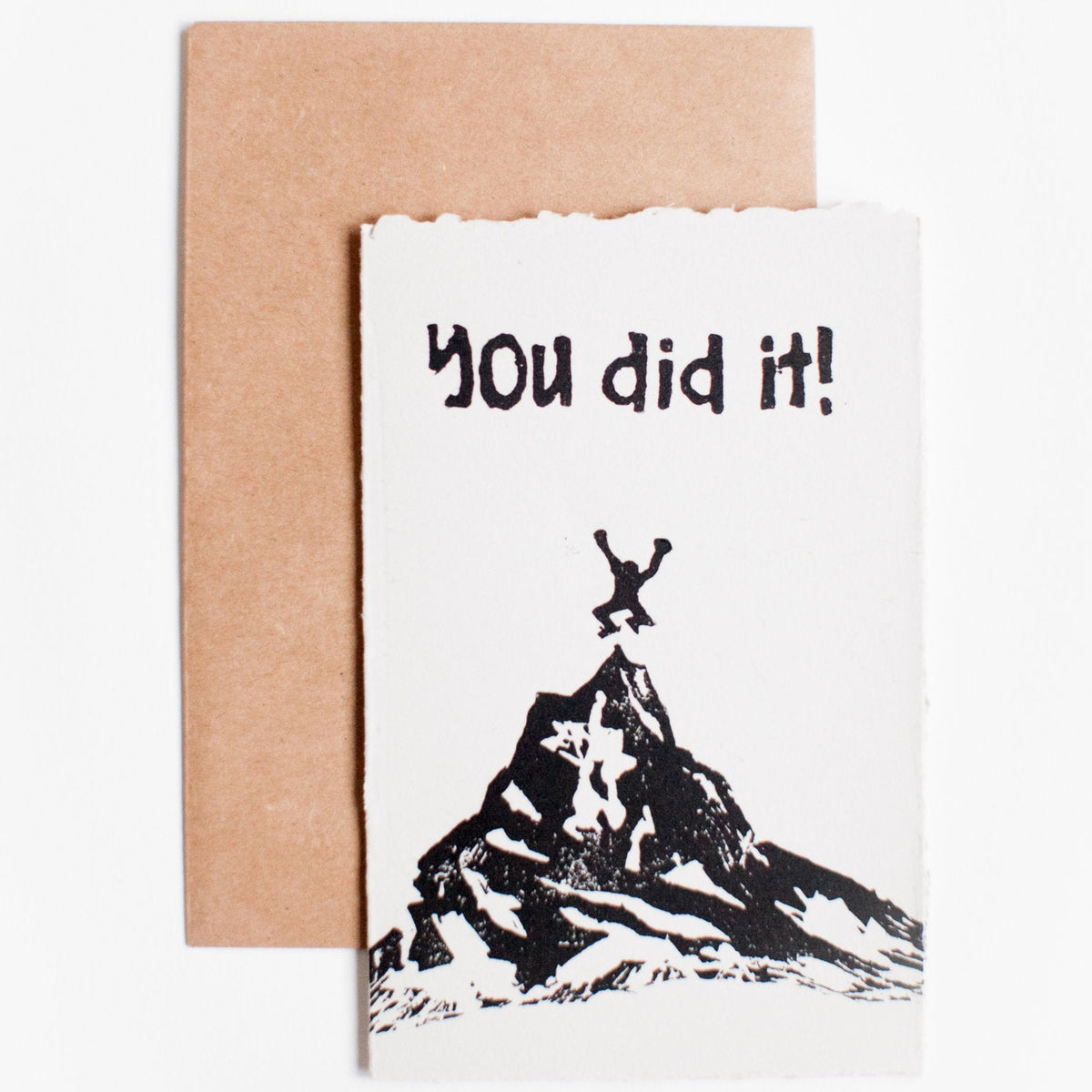 4x6 hand carved and pressed black and white card reading "you did it!" with a person jumping on a mountain top