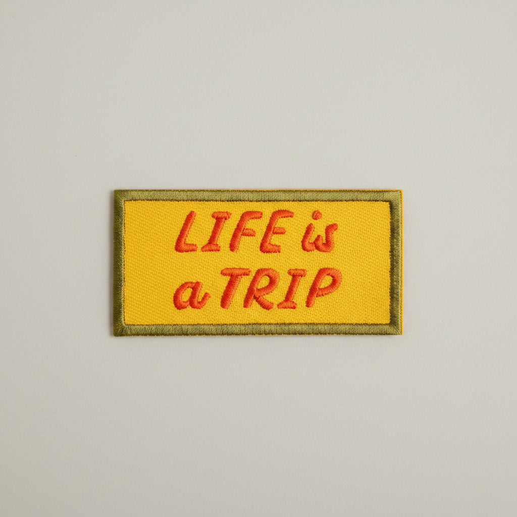 Rectangular shaped iron-on patch with a yellow background and red words that say "Life is a trip".