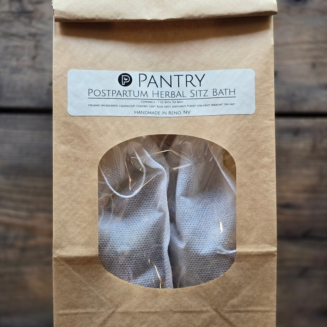 Paper bag with clear front showing herbal sachets inside. Soft natural label with blank font, product shown against wooden table.