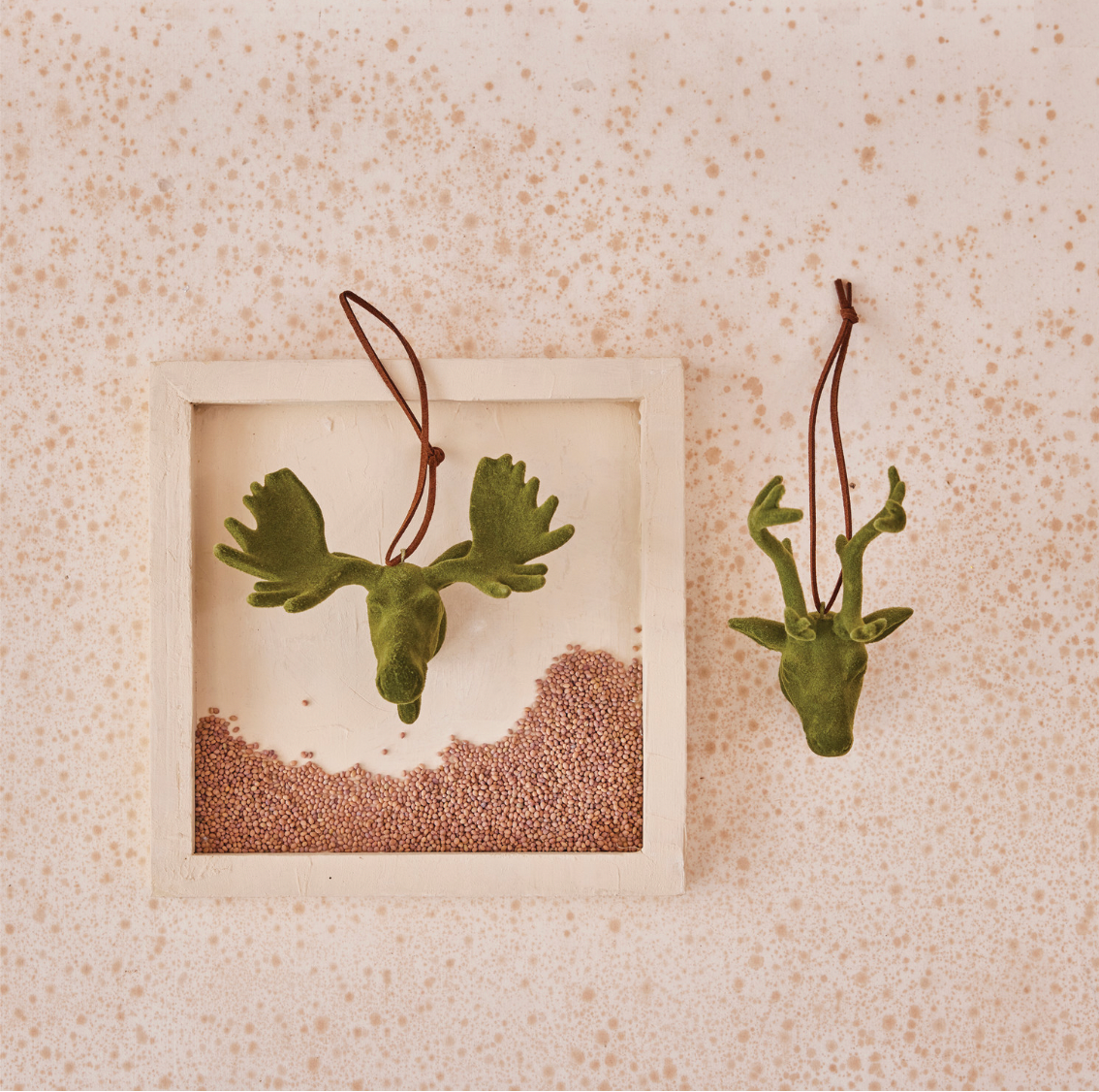 Green deer head & moose head ornaments hanging on a textured beige wall.