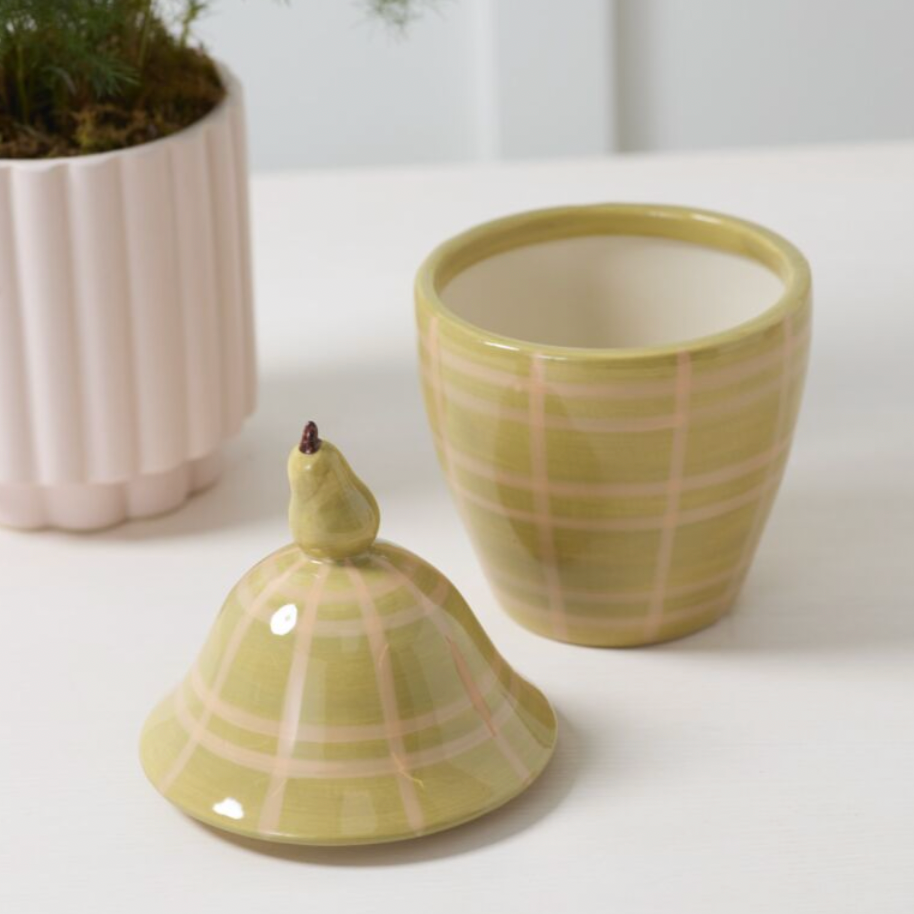 Green ceramic container with plaid pattern and a small pear-shaped object on top, next to a similar container.