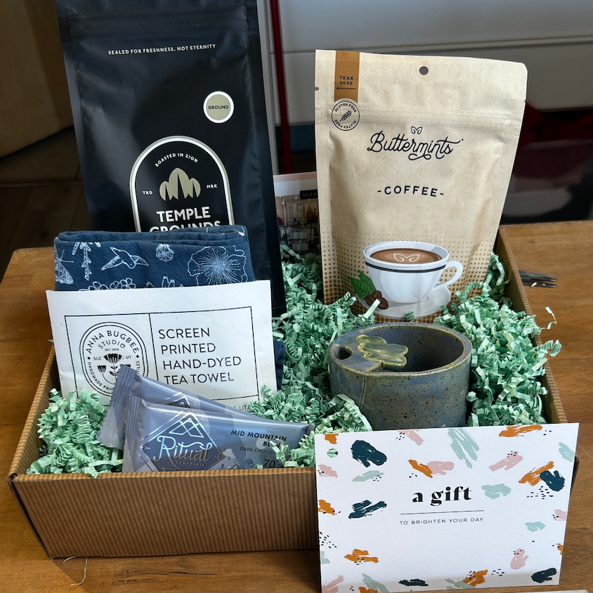 Gift basket with coffee, tea towel, and cards on a wooden surface