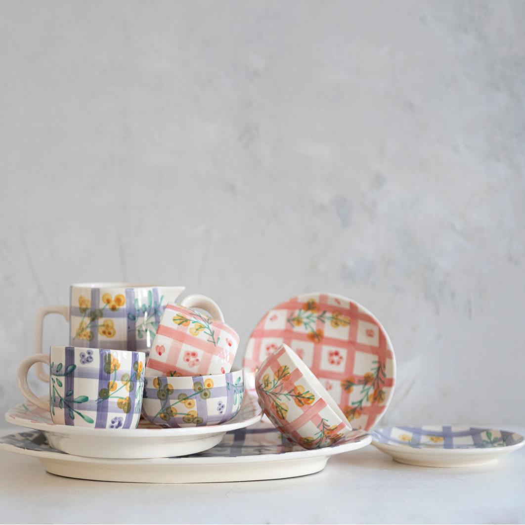 Set of ceramic cups and saucers with floral and checkered patterns on a light gray background