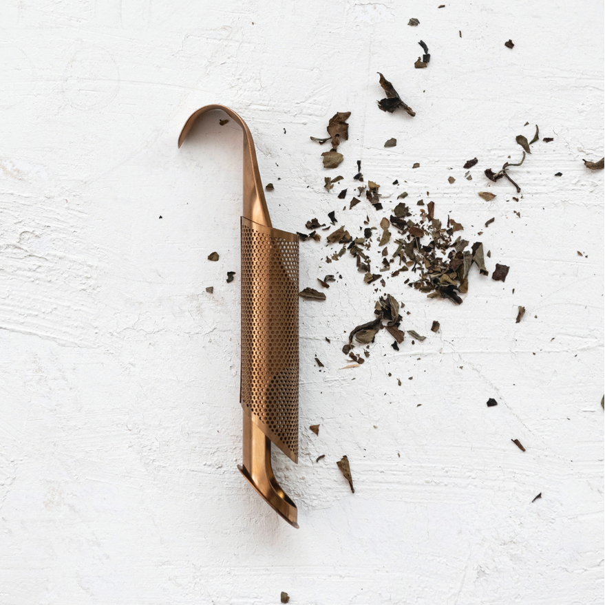 Tea infuser with tea leaves on a white surface