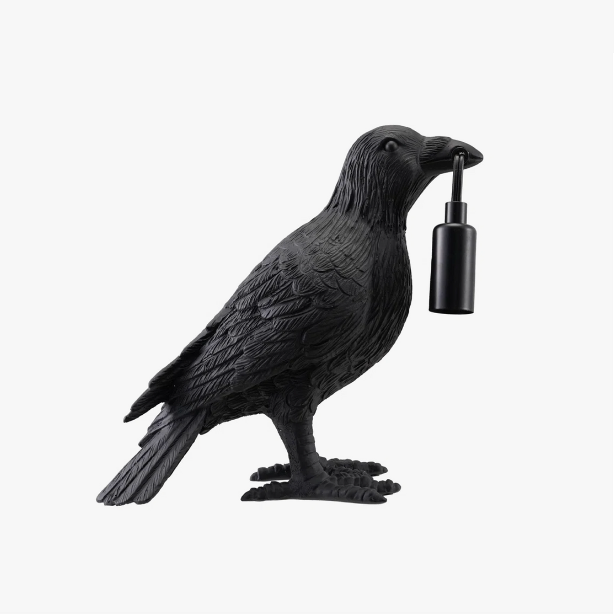 A black raven figurine holding a small black cylindrical light in its beak, photographed against a plain light gray background.