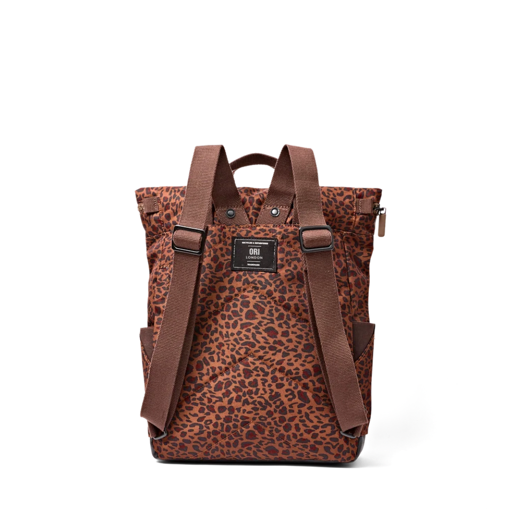 A brown and black leopard print backpack with brown leather straps and a black brand patch on the front, photographed on a clean white background.