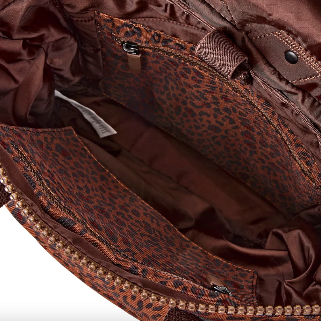 Close-up of the interior of a brown leopard-print bag, showing multiple zippered compartments and a satin lining.