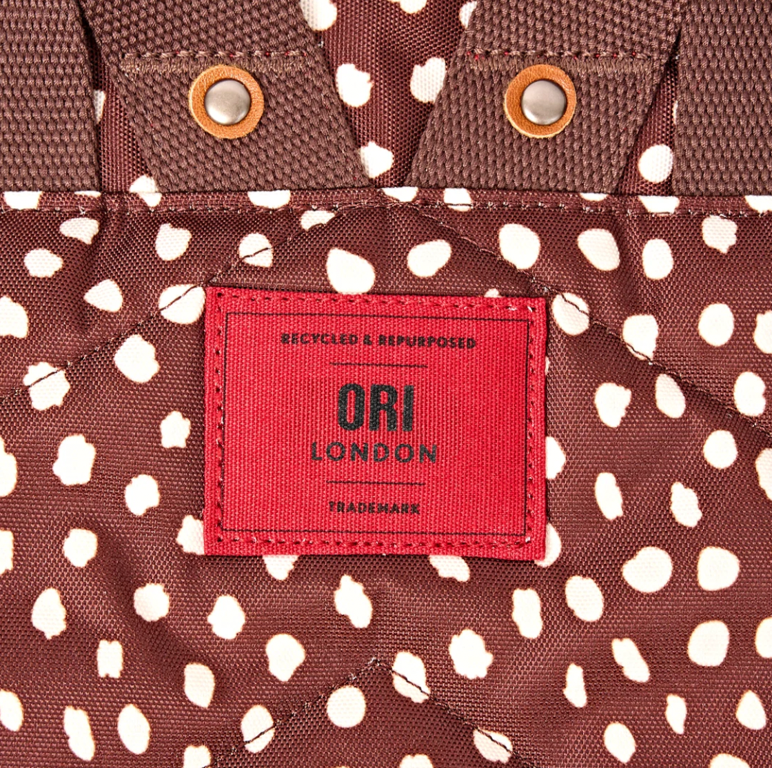 Close-up of a brown and white spotted backpack with a red ORI LONDON patch label.