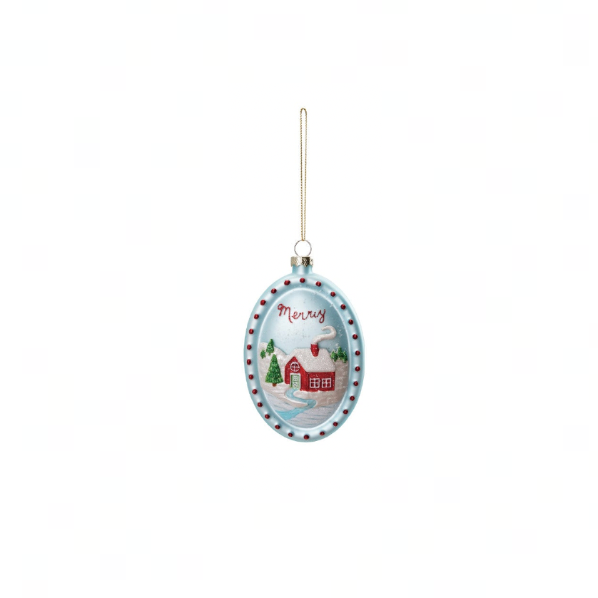 An oval Christmas ornament featuring a winter scene with a red cabin, snow, evergreen trees, and the word 'Merry' on a light blue background, hanging from a thin gold string against a white background.