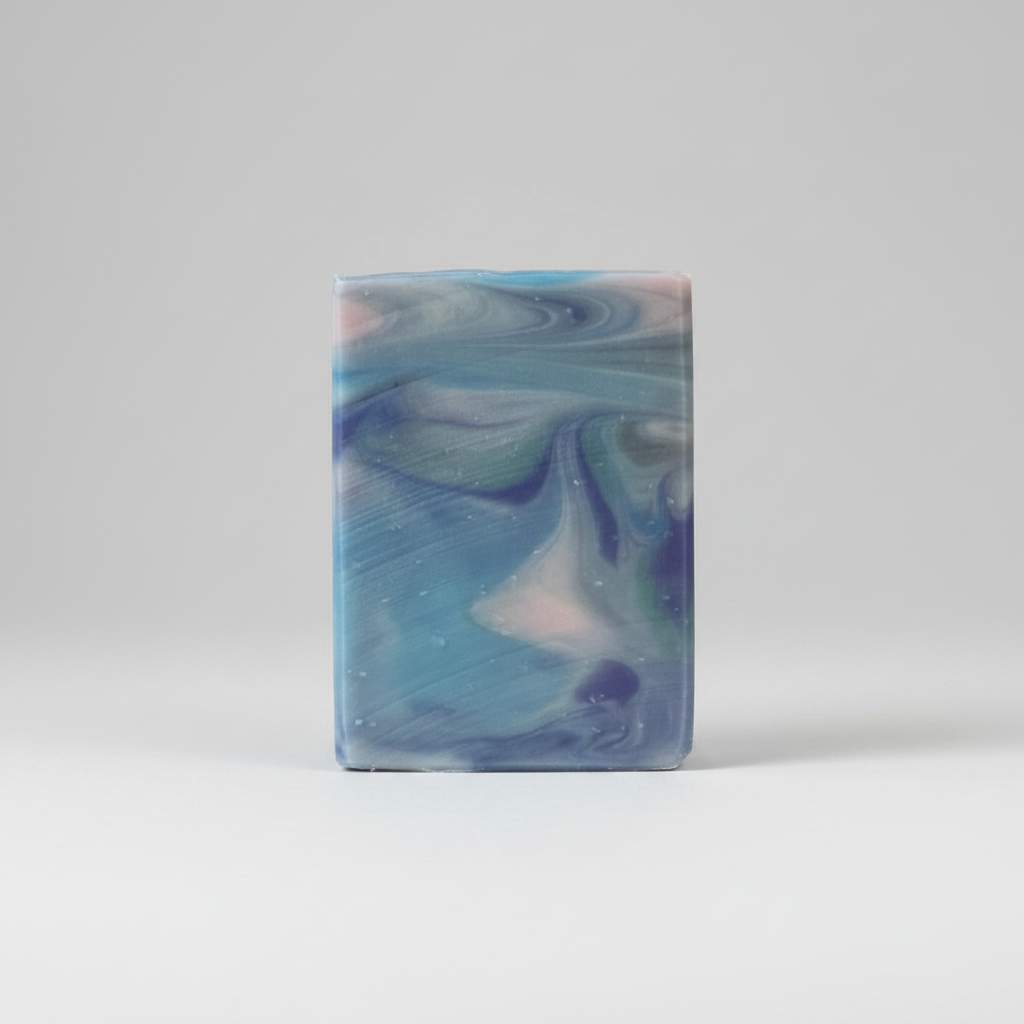A rectangular bar of marbled soap in shades of blue, teal, and lavender, displayed on a circular wooden coaster against a purple and blue starry sky background.
