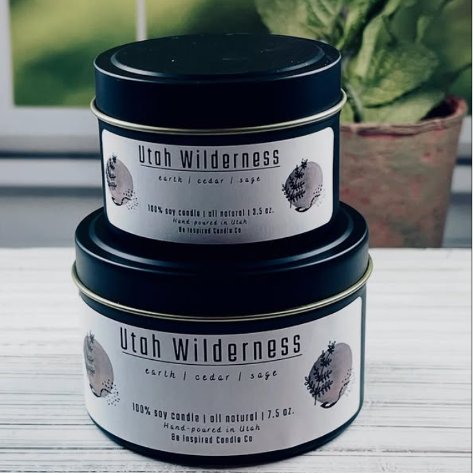 Two Utah Wilderness candles stacked on a surface with a blurred plant in the background