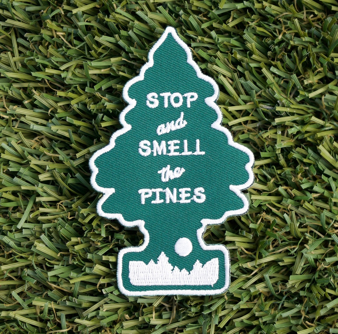 Iron-on embroidered patch with the shape of a pine tree and the words "Stop and smell the pines".