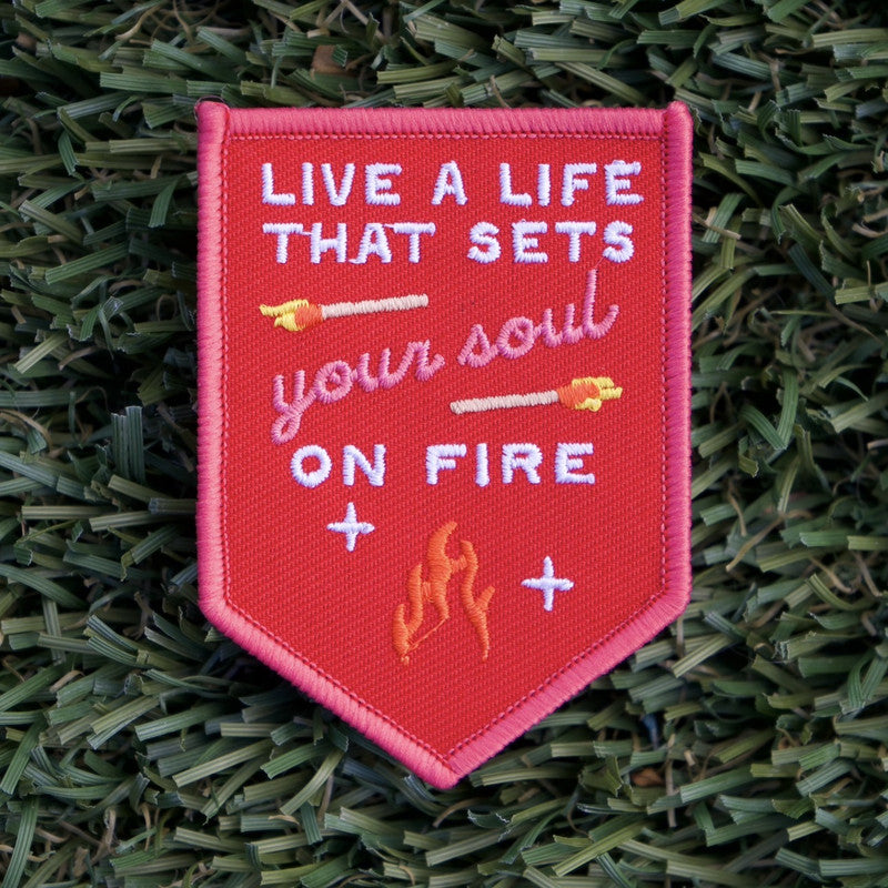 Red iron-on patch with the embroidery of two little matches and a fire flame, and the words in white "Live a life that sets your soul on fire".