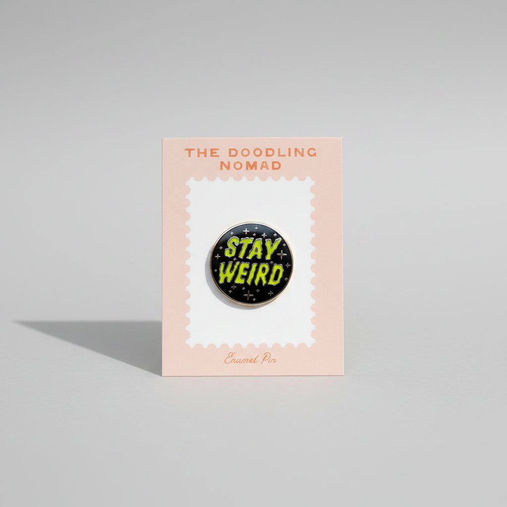 Circle-shaped enamel pin with black background and green words that say "Stay Weird" in green.