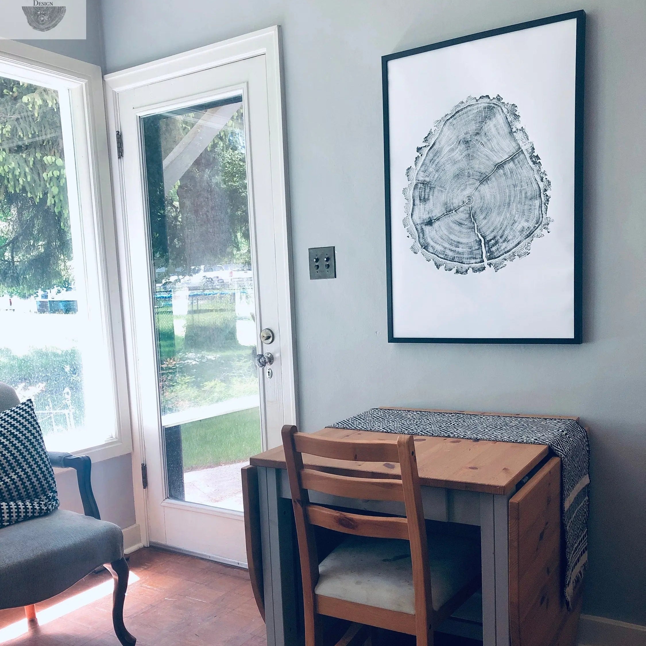Small dining area with a wooden table and chairs against a light blue wall with a framed picture.