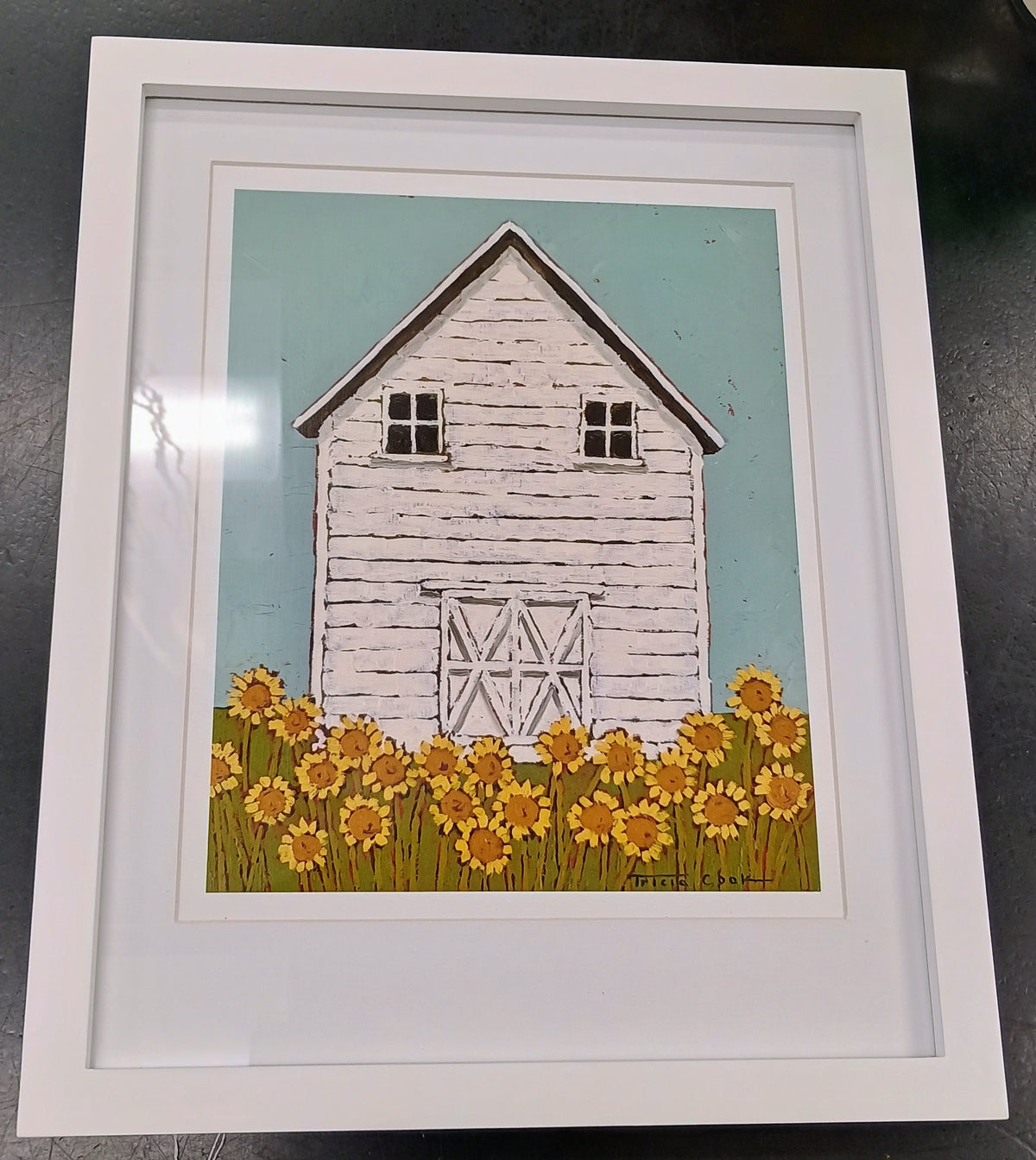 Framed print of rustice white barn, with ligth blue sky, and yellow sunflowers in the foreground.