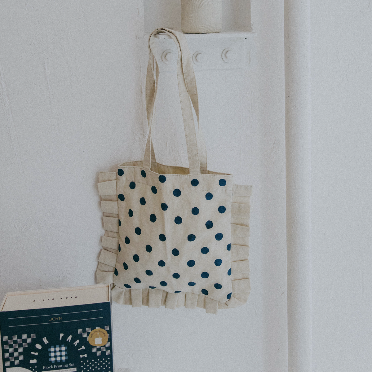 Tote bag with polka dot pattern hanging on a white wall next to a book.