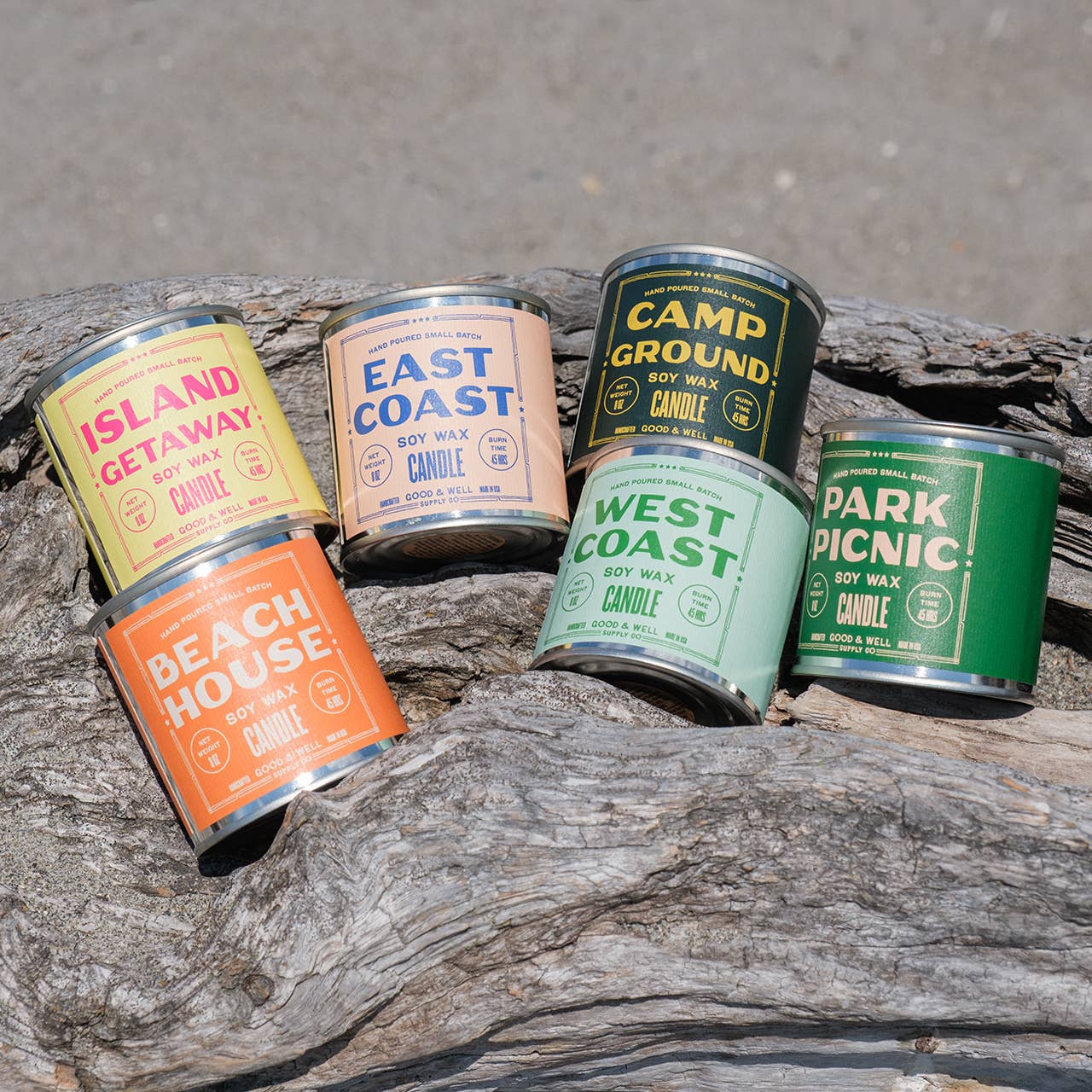 Set of six candles in metal cans with different designs and text on a wooden surface.