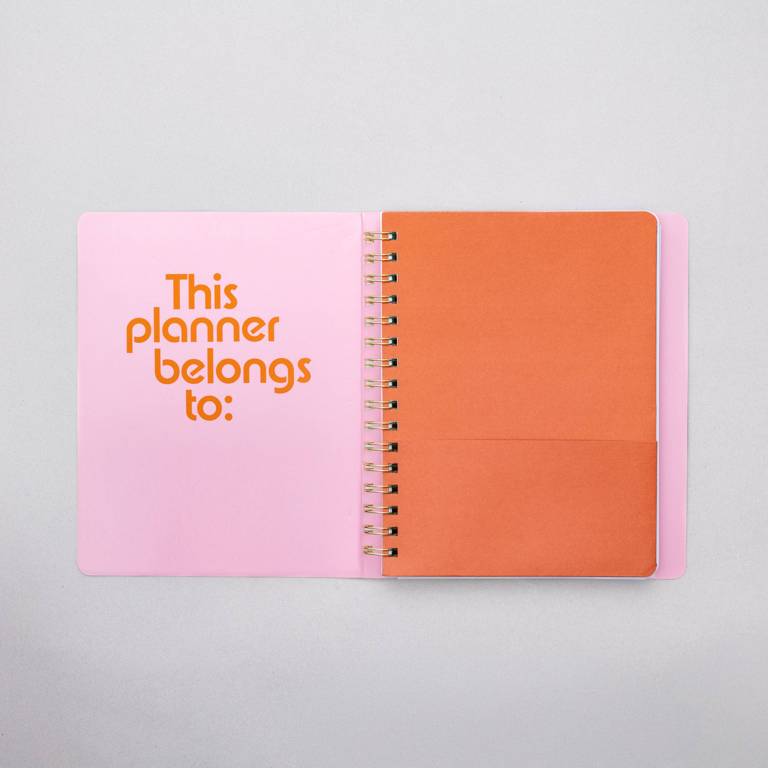 Open planner with pink cover and orange interior on a light gray background