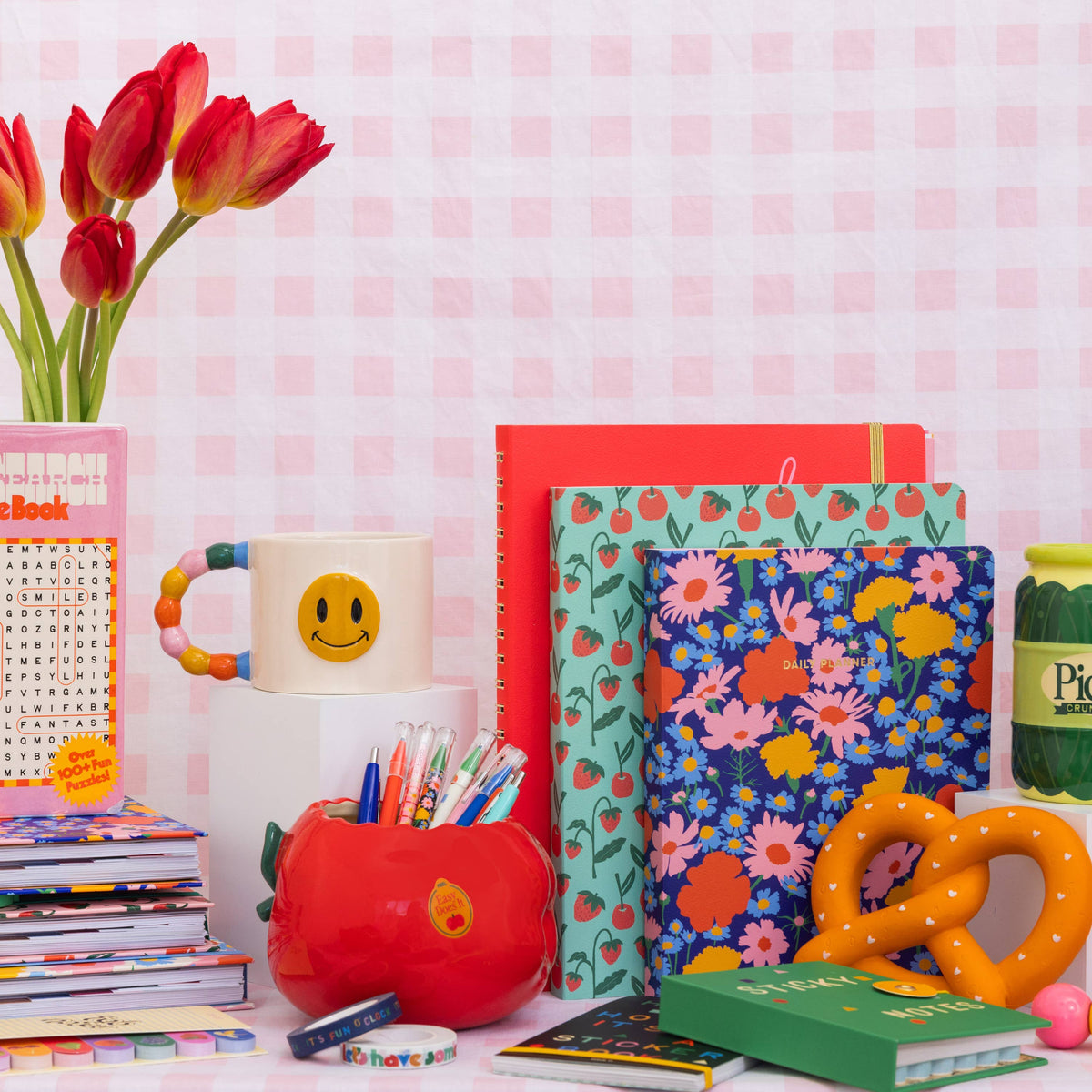 Colorful stationery items including notebooks, mugs, and flowers on a checkered background