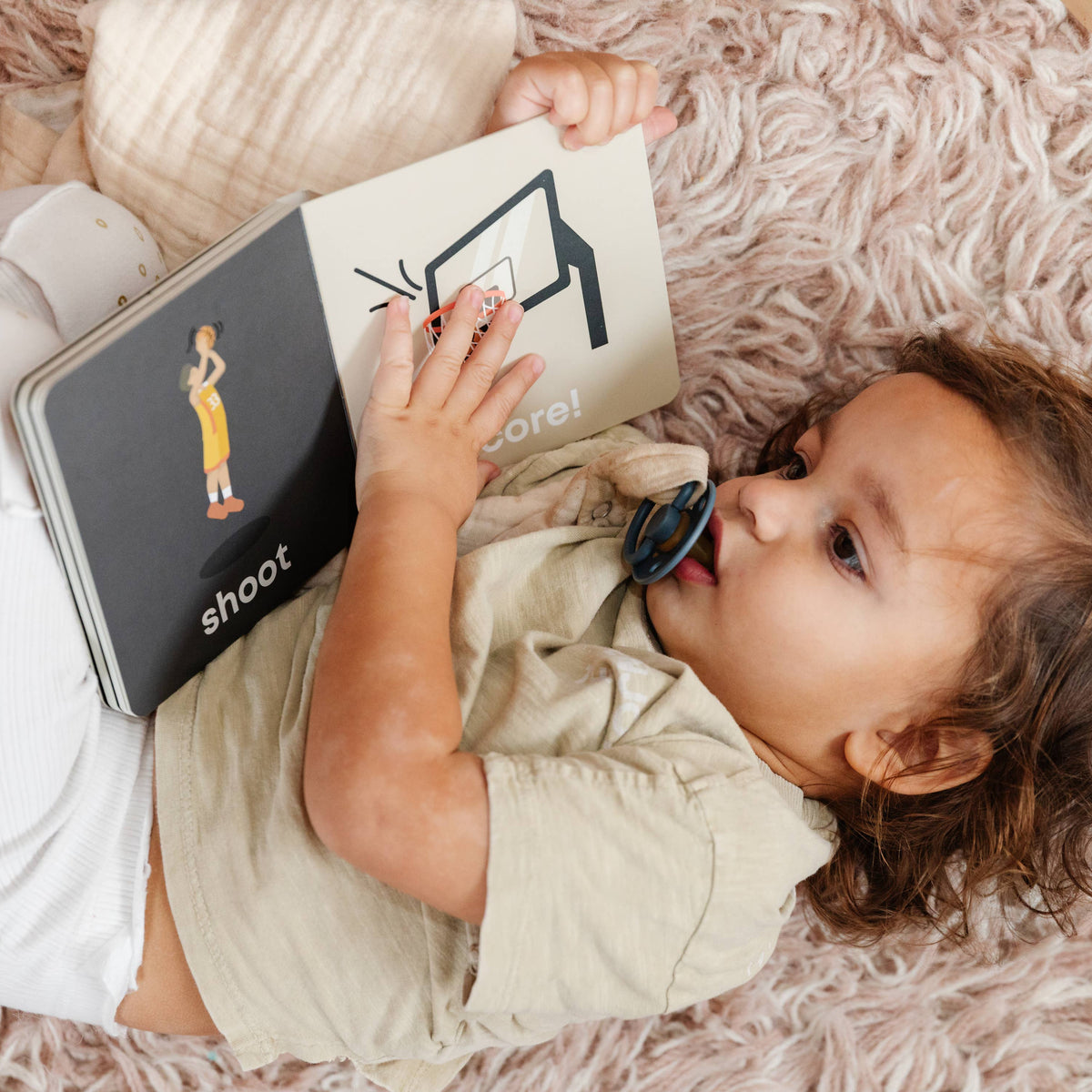 Child lying on a fluffy pink rug reading a book with 'shoot' branding.